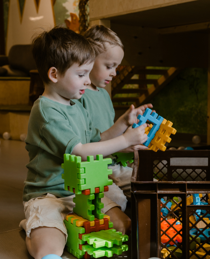 Two children playing with colorful building blocks in a hotel play area, surrounded by soft play balls.