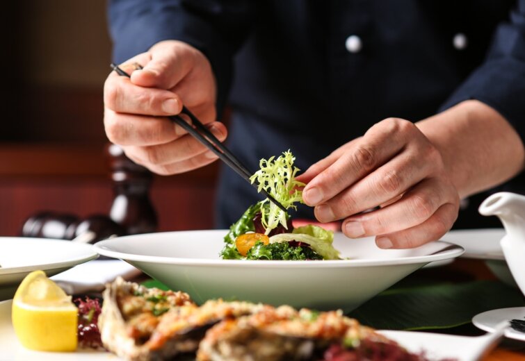 Šéfkuchař pečlivě zdobí čerstvý zelený salát v elegantním hotelovém prostředí.