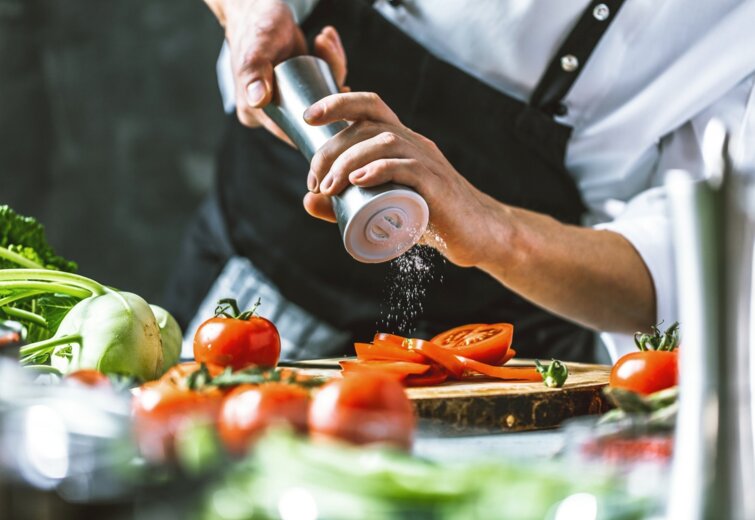 Šéfkuchař dochucuje čerstvě nakrájená rajčata na dřevěném prkénku v profesionální hotelové kuchyni