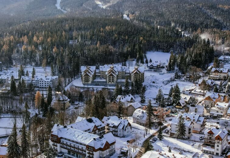 Zimní pohled na zasněžené městečko s hotely pod lesnatými horami a lyžařskými sjezdovkami.
