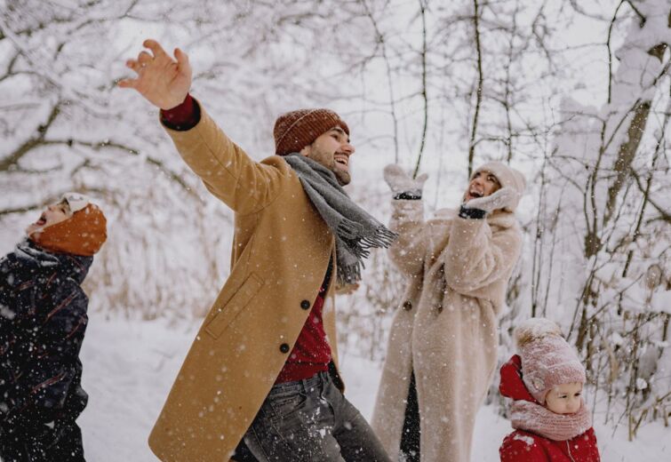 Family enjoying playful snowtime outdoors in warm winter clothes amid a snowy forest setting