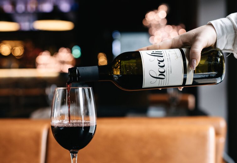 Servírka nalévá červené víno do sklenice v útulné, elegantní restauraci s teplým osvětlením