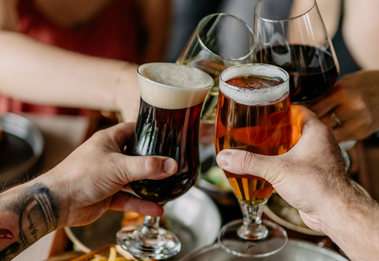 Hosté v hotelové restauraci přípitkují pivem a vínem u talíře s řízkem, smaženým vejcem, hranolkami a zelným salátem.