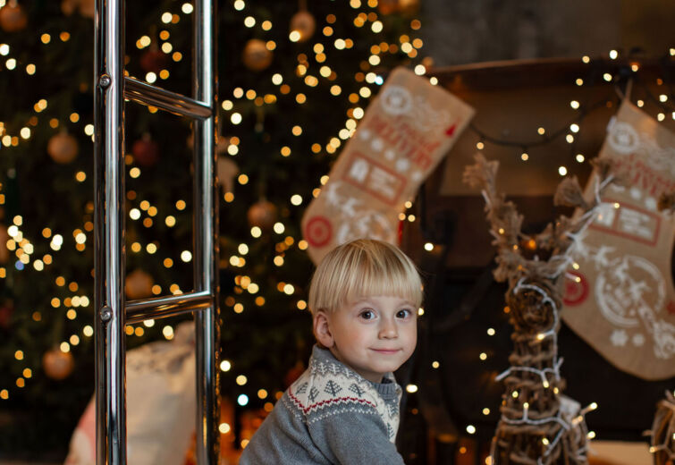 Mały chłopiec bawi się na hotelowym wózku bagażowym przy świątecznie oświetlonej choince i dekoracjach świątecznych.