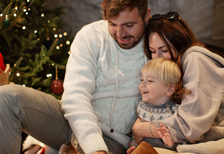 Rodzina bawiąca się z psem w przytulnym wnętrzu obok świątecznie udekorowanej choinki