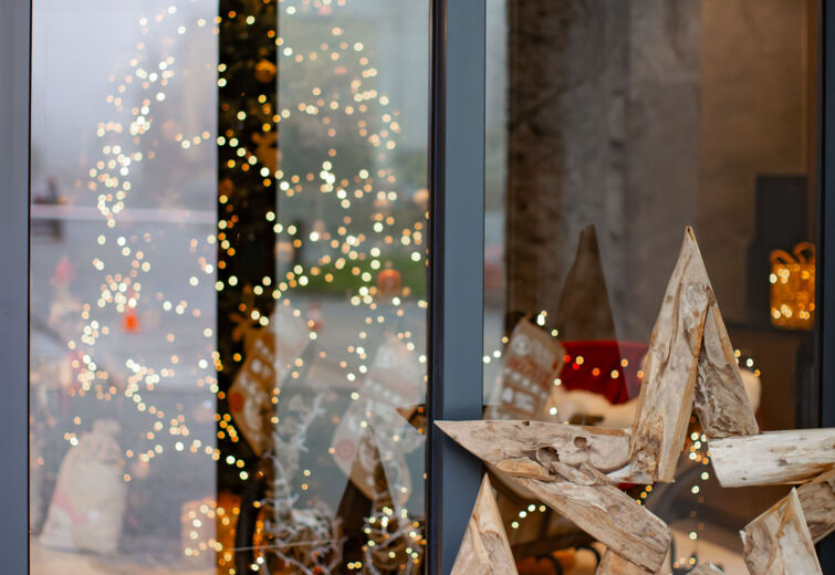 Drewniane gwiazdy stojące przy szklanych drzwiach z odbiciem świątecznych dekoracji i migoczących światełek