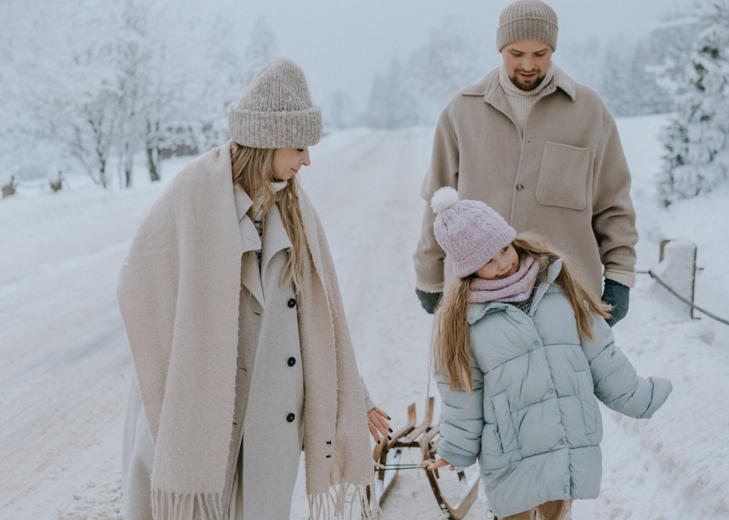 Family dressed in warm winter clothes walking on a snowy road in a scenic mountain winter landscape.