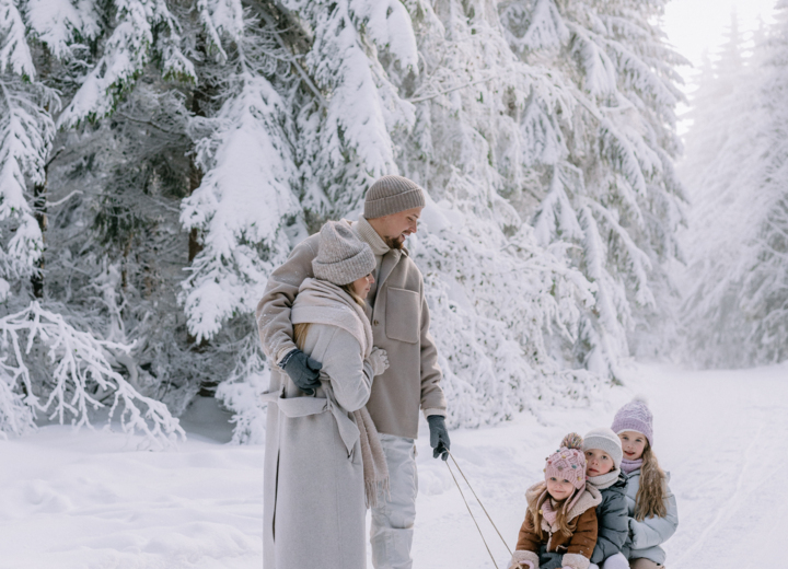 Familie in Wintermänteln genießt eine Schlittenfahrt auf einem verschneiten Waldweg mit schneebedeckten Bäumen.