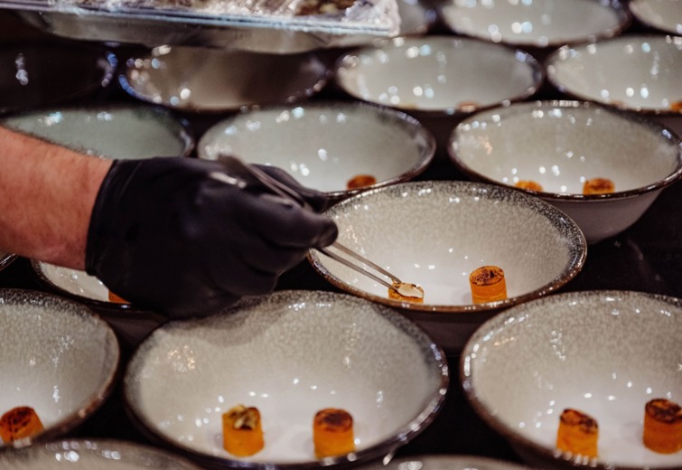 Chef wearing black glove artfully places small gourmet dishes in textured ceramic bowls.