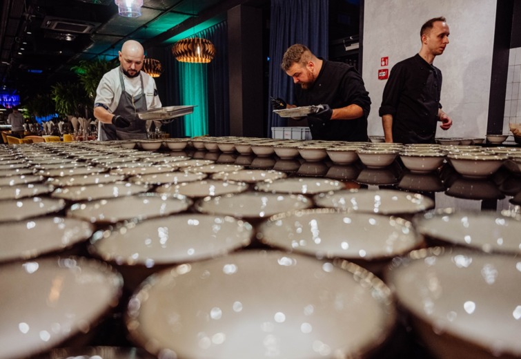 Chefs preparing numerous bowls neatly arranged on a long table in a modern restaurant setting