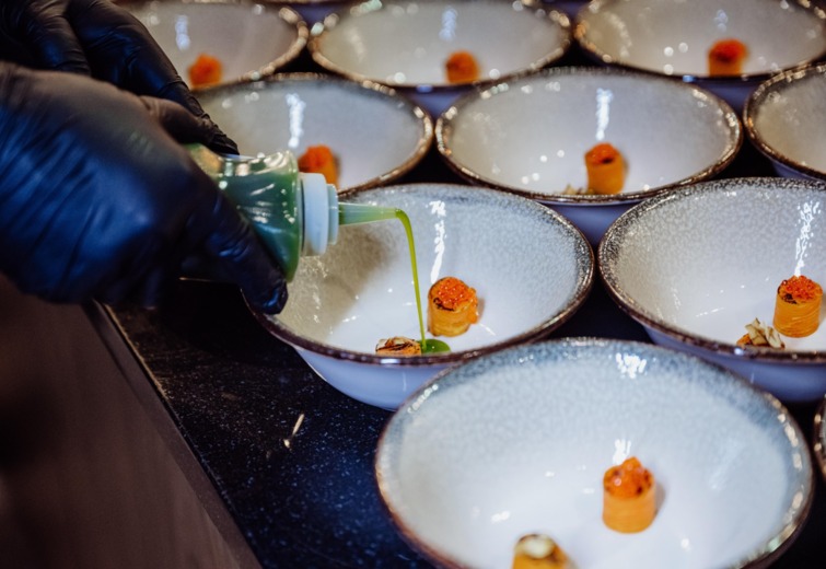 Chef wearing gloves pours green sauce into stylish bowls with delicately prepared appetizers