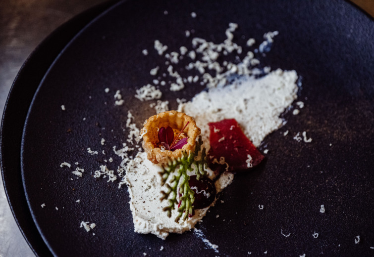 Gourmet appetizer with crispy tart, creamy sauce, red gel, and edible leaf on a black plate