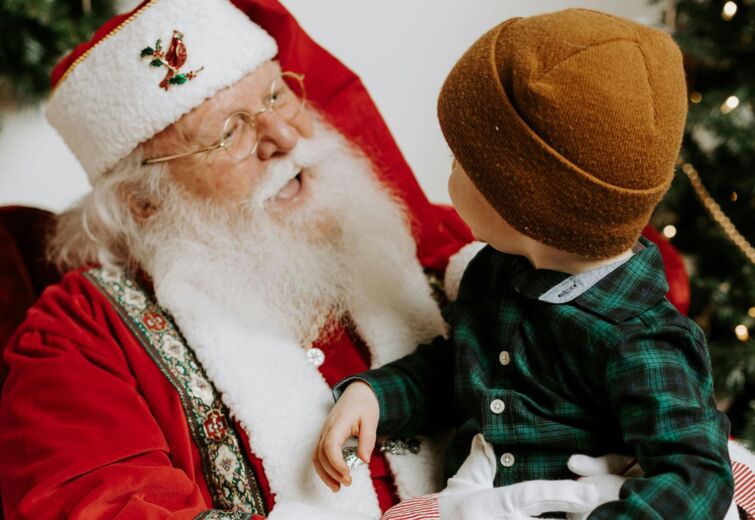 Wesoły Święty Mikołaj rozmawia z małym chłopcem przy udekorowanej choince w świątecznym wnętrzu hotelu.