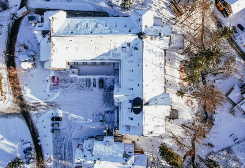 Hotel położony w zimowym krajobrazie z ośnieżonym dachem i pobliskimi domami oraz zadaszonym parkingiem