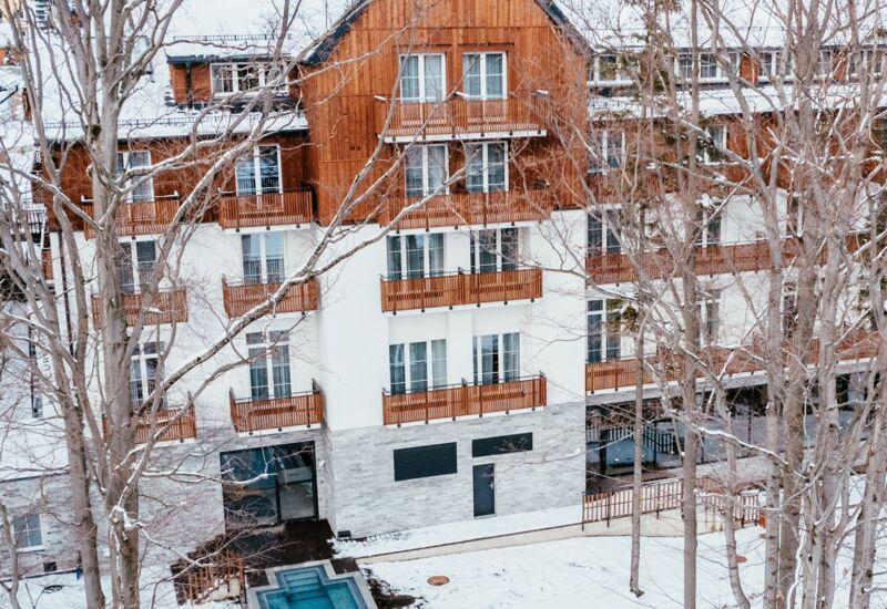 Hotel w zimowej scenerii z drewnianą elewacją, balkonami i niewielkim podgrzewanym basenem na zewnątrz