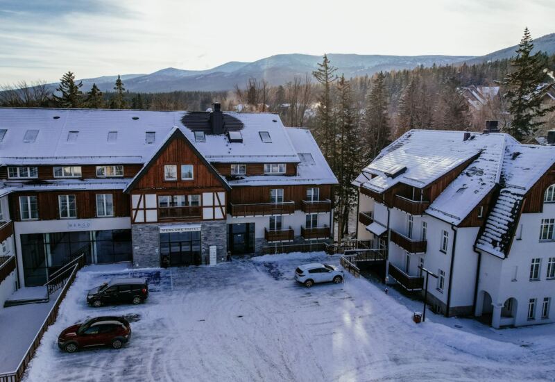 Hotel Mercure z drewnianymi balkonami otoczony śniegiem, z widokiem na ośnieżone góry i lasy w tle.