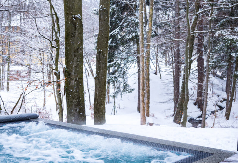 Podgrzewany jacuzzi na zewnątrz z bąbelkami otoczony śnieżnym lasem zimą