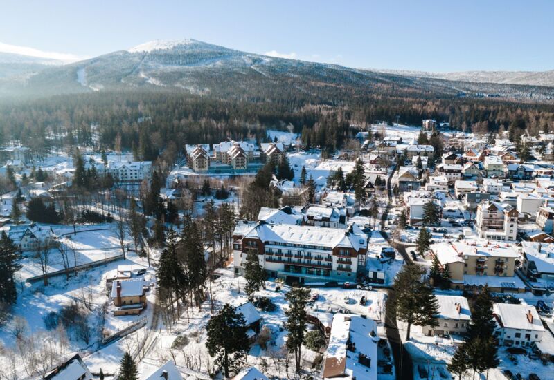 Zimowy widok na górskie miasteczko z hotelami, lasem i szczytem pokrytym śniegiem w tle