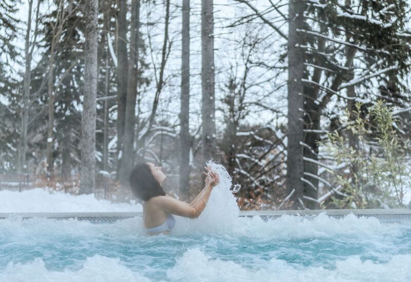 Kobieta relaksująca się w zewnętrznym jacuzzi otoczonym śnieżnym lasem zimą