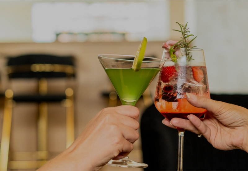Zwei Gäste stoßen mit bunten Cocktails in einer eleganten Hotelbar an.
