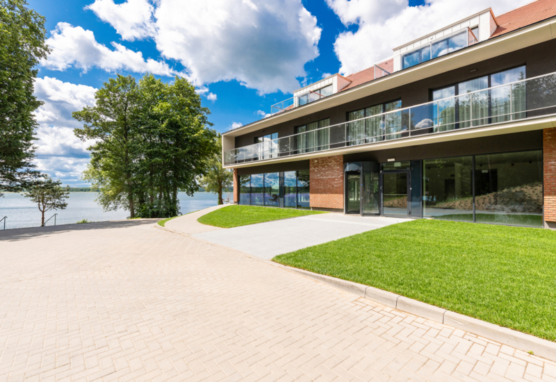 Nowoczesny hotel nad jeziorem z dużymi oknami, balkonami i zielonym terenem rekreacyjnym przy wodzie