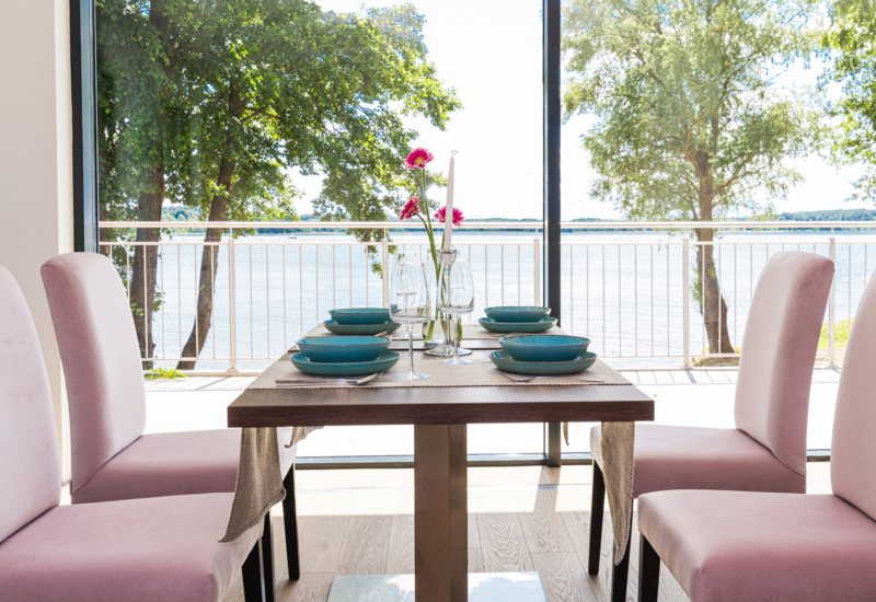 Jadalnia z różowymi krzesłami i stołem nakrytym niebieską zastawą, z widokiem na wodę i drzewa za dużymi oknami.