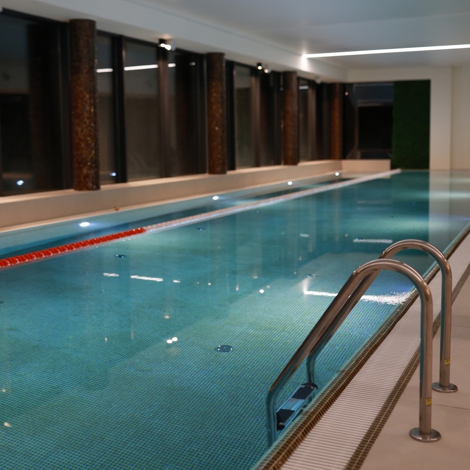 An indoor hotel swimming pool with turquoise water, a metal handrail, and a calm wellness area interior. The space encourages relaxation during the stay.