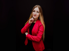 Žena v rudém saku na černém pozadí, profesionální portrét, přátelský sebevědomý úsměv, sepjaté paže, ruka u brady