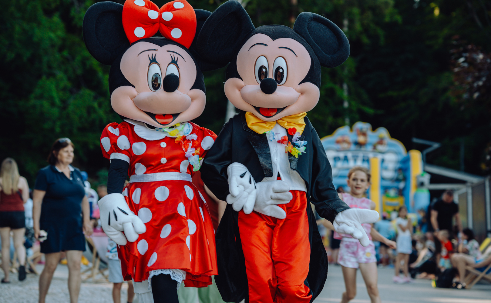 Przebrane maskotki Minnie i Mickey idą za ręce podczas rodzinnej, pełnej zabawy imprezy w kurorcie.