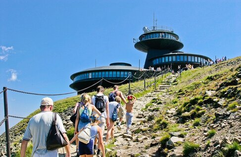 Goście podchodzą kamienistą ścieżką do okrągłego górskiego hotelu z panoramicznymi oknami i tarasem widokowym