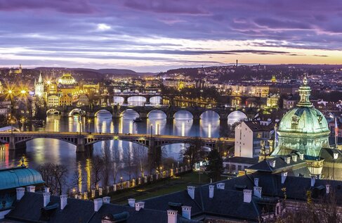 Panoramiczny wieczorny widok z tarasu hotelowego na rzekę, zabytkowe kamienne mosty i oświetloną panoramę miasta z kopułą