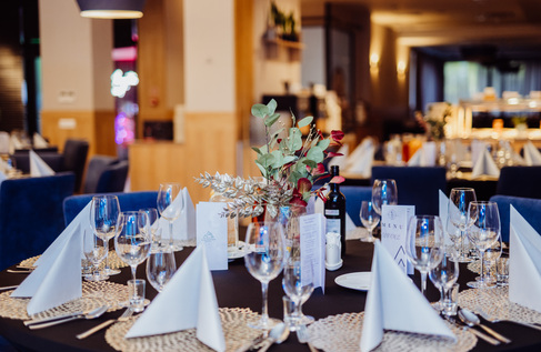 Elegantně prostřený stůl v hotelové restauraci na večeři se složenými bílými ubrousky, vinnými sklenicemi, lahví vína a listovou dekorací.