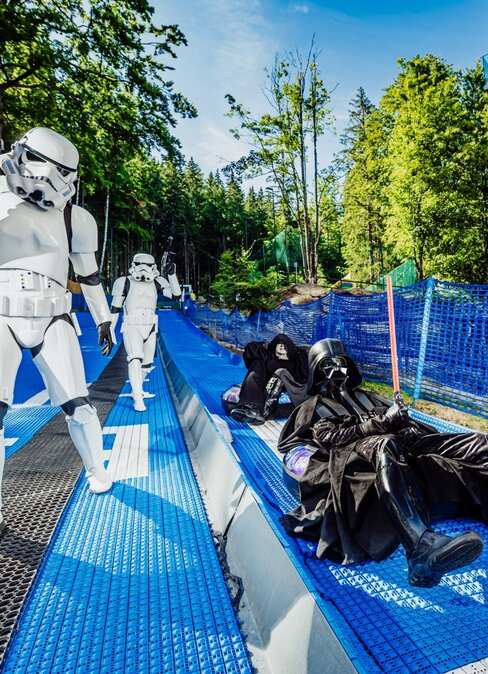 Guests in Star Wars costumes on a blue summer tubing run next to a modern hotel and wooded hillside