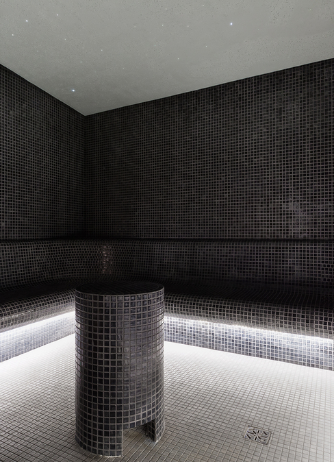 Mosaic-tiled hotel steam room with curved bench seating, central stool, subtle under-bench LED lighting and starry ceiling