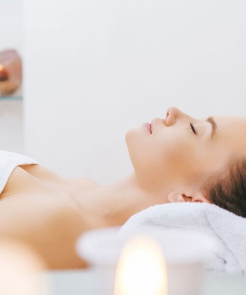 Kobieta relaksuje się na leżance spa w ręczniku, przy miękkim świetle świec i aromaterapii w spokojnym gabinecie