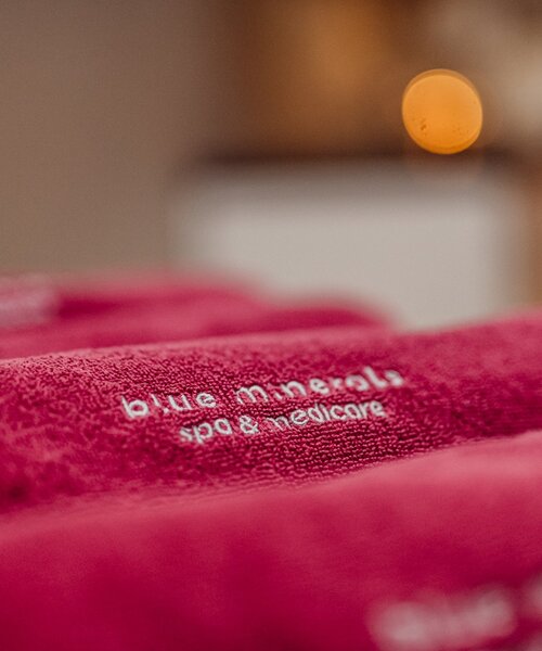 Różowe, miękkie ręczniki spa z haftem 'blue minerals spa & medicare', przytulne, rozmyte światło w tle