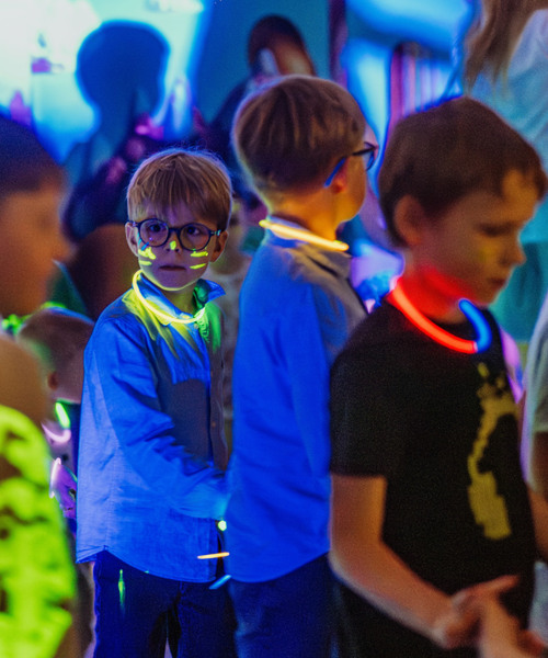 Dzieci na hotelowej glow-party w klubie dziecięcym, w świecących naszyjnikach i malowaniu twarzy.