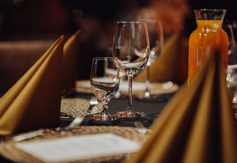 Elegancko nakryty stolik w restauracji z kieliszkami do wina i wody, musztardowymi serwetkami i karafką soku pomarańczowego