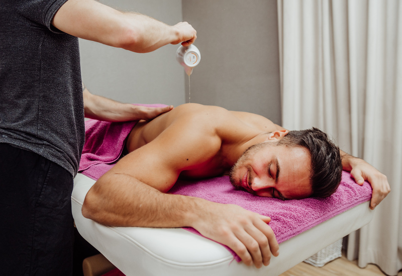 Mężczyzna otrzymuje relaksacyjny masaż pleców z olejkiem na stole spa, terapeuta wylewa olej
