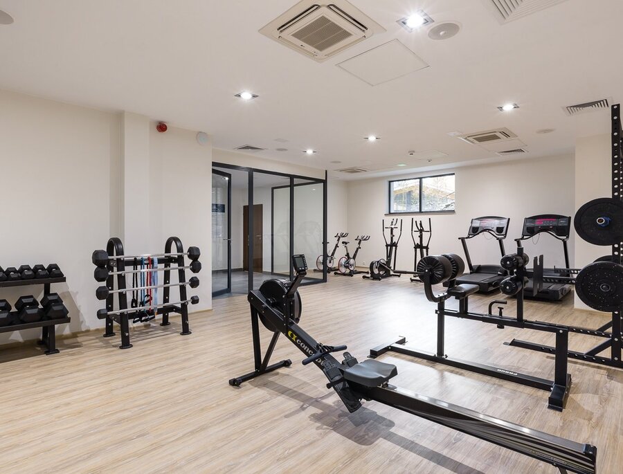 Moderní hotelové fitness s veslařským trenažérem, běžeckými pásy, stacionárními koly, lavicí a stojany s kotouči a jednoručkami