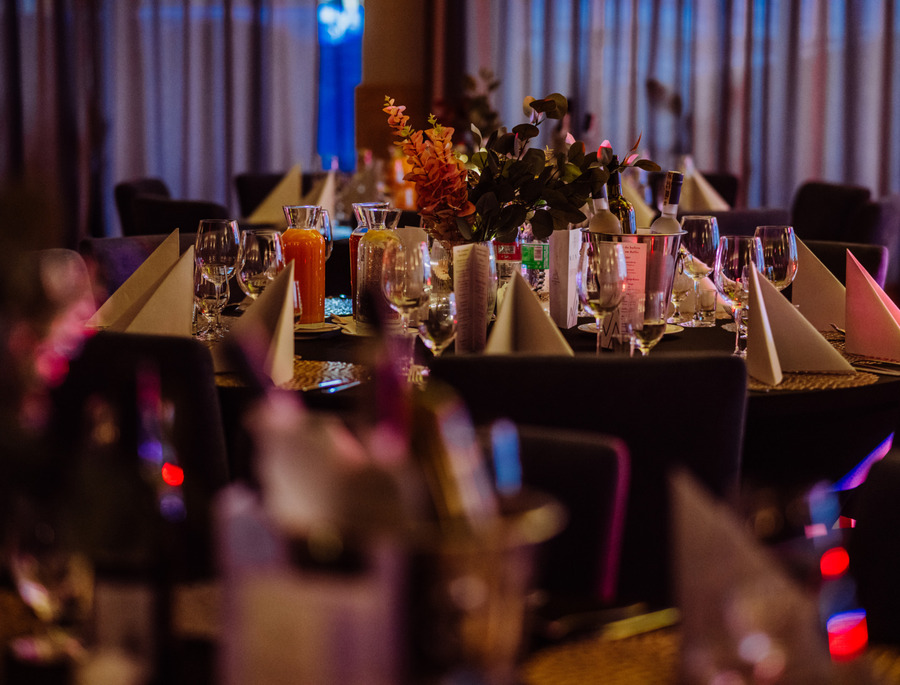 Bankett-Tisch mit gefalteten Servietten, Weingläsern, Saftkaraffen, Blumenarrangement und Wein im Eiseimer, warmes Licht