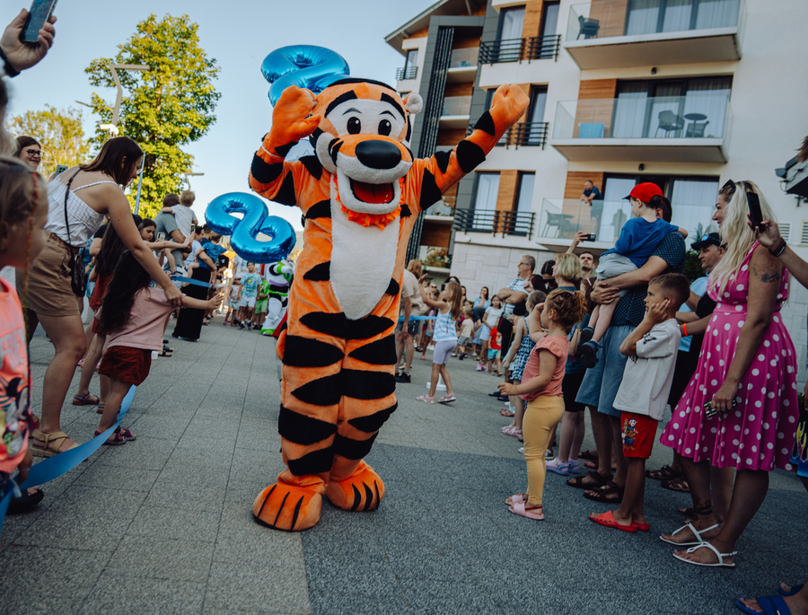 Familienevent im Hotel mit Tiger-Maskottchen, das Kinder vor modernen Balkonen unterhält.