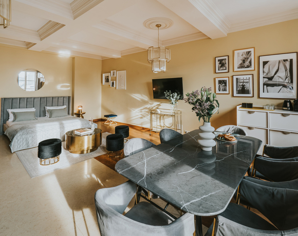 Przestronny apartament typu studio z łóżkiem king, welurowym zagłówkiem, marmurowym stołem, złotymi akcentami, telewizorem, kwiatami i ekspresem do kawy