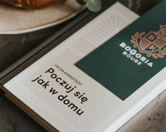 Branded Bogoria House welcome card resting on a guest information book reading 'poczuj się jak w domu', warm upscale welcome.