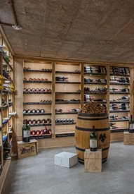 Hotel wine cellar with wood racks of backlit bottles, cork-topped barrel centerpiece and intimate tasting ambiance.