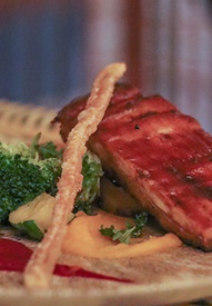 Glazed grilled pork belly with seasonal broccoli, zucchini, red pepper purée and crisp breadstick on a ceramic plate
