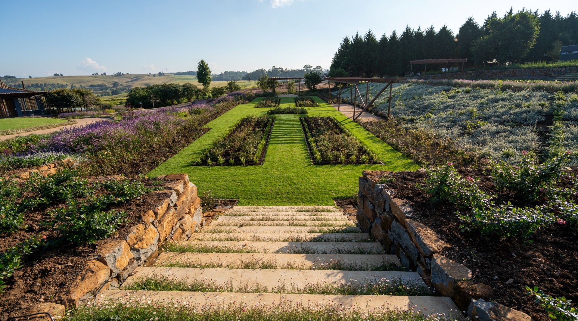 Terraced hotel gardens with stone steps leading to lawns, lavender beds, pergola walkway and rolling countryside views.