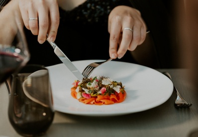 Hands using knife and fork to cut a delicate smoked-salmon appetizer garnished with microgreens and edible flowers, fine-dining.