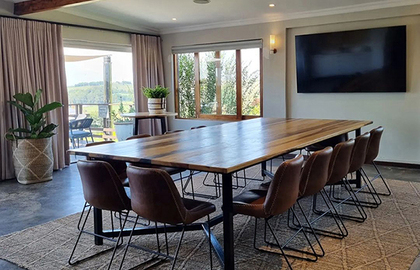 Boardroom-style meeting room with long wooden table, leather chairs, wall TV, exposed beam, woven rug and terrace views
