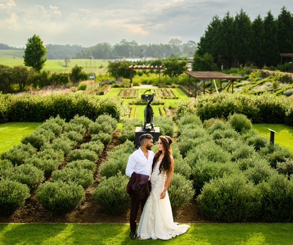 Newlyweds in a manicured herb garden with sculpture, pergolas and rolling countryside — elegant wedding venue.